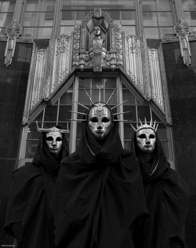 Zespół "Imperial Triumphant", Postacie w czarnych płaszczach i z łotych maskach.