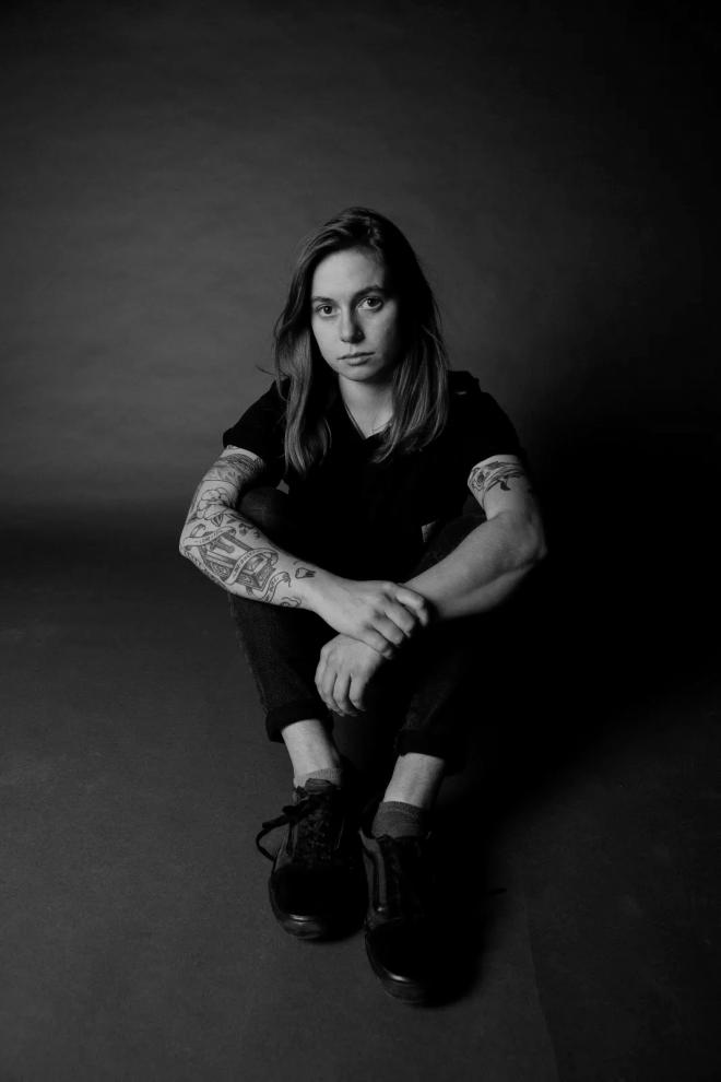 Julien Baker siedzi na podłodze, patrzy w obiektyw.